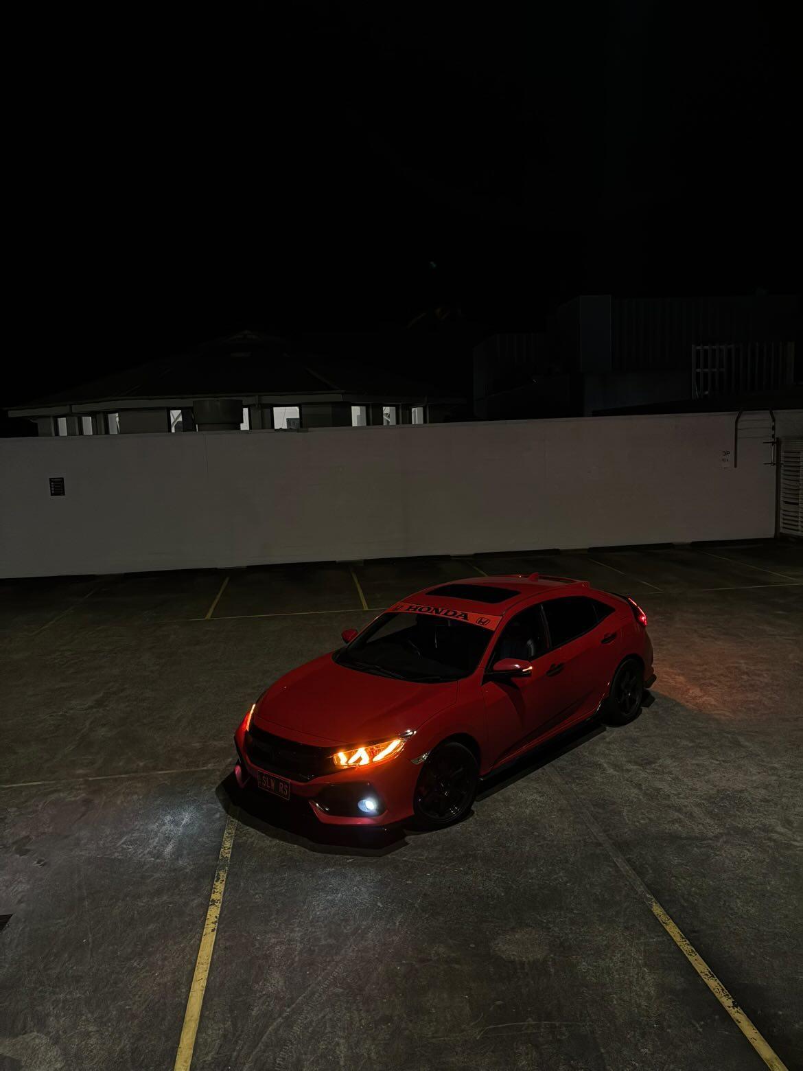 Red Honda Civic hatchback parked at night, front three-quarter view