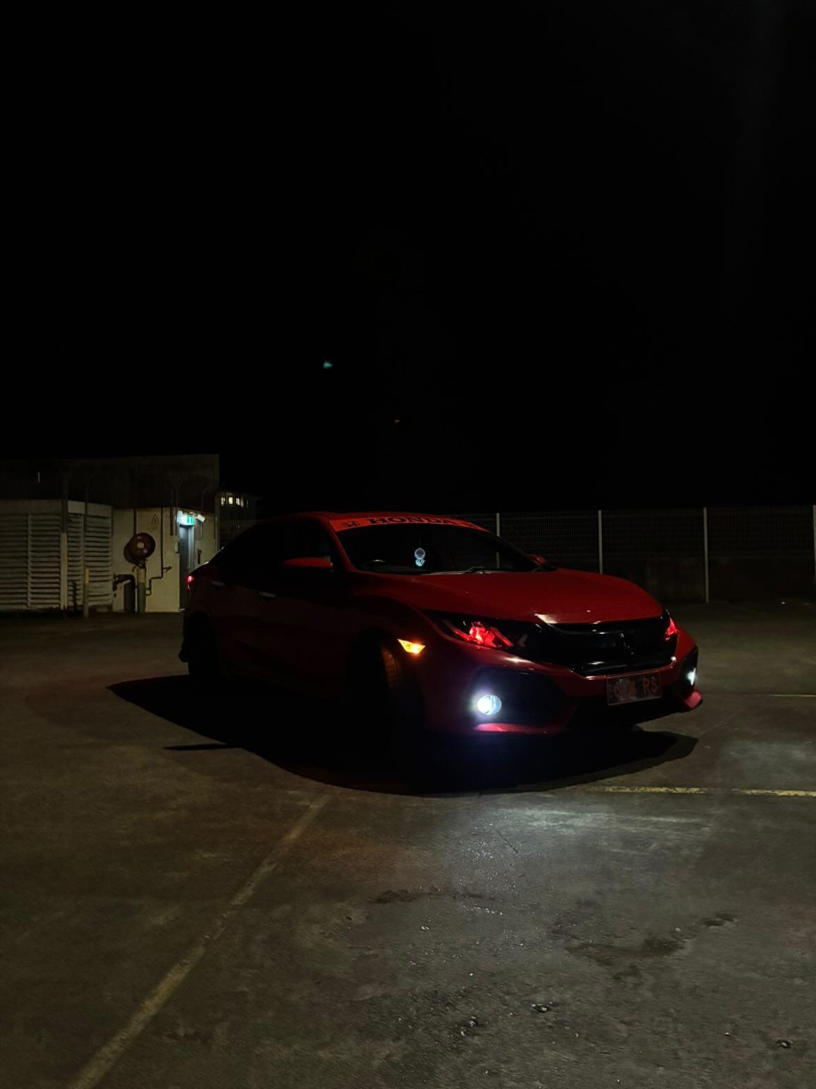 Red Honda Civic hatchback parked at night, front view