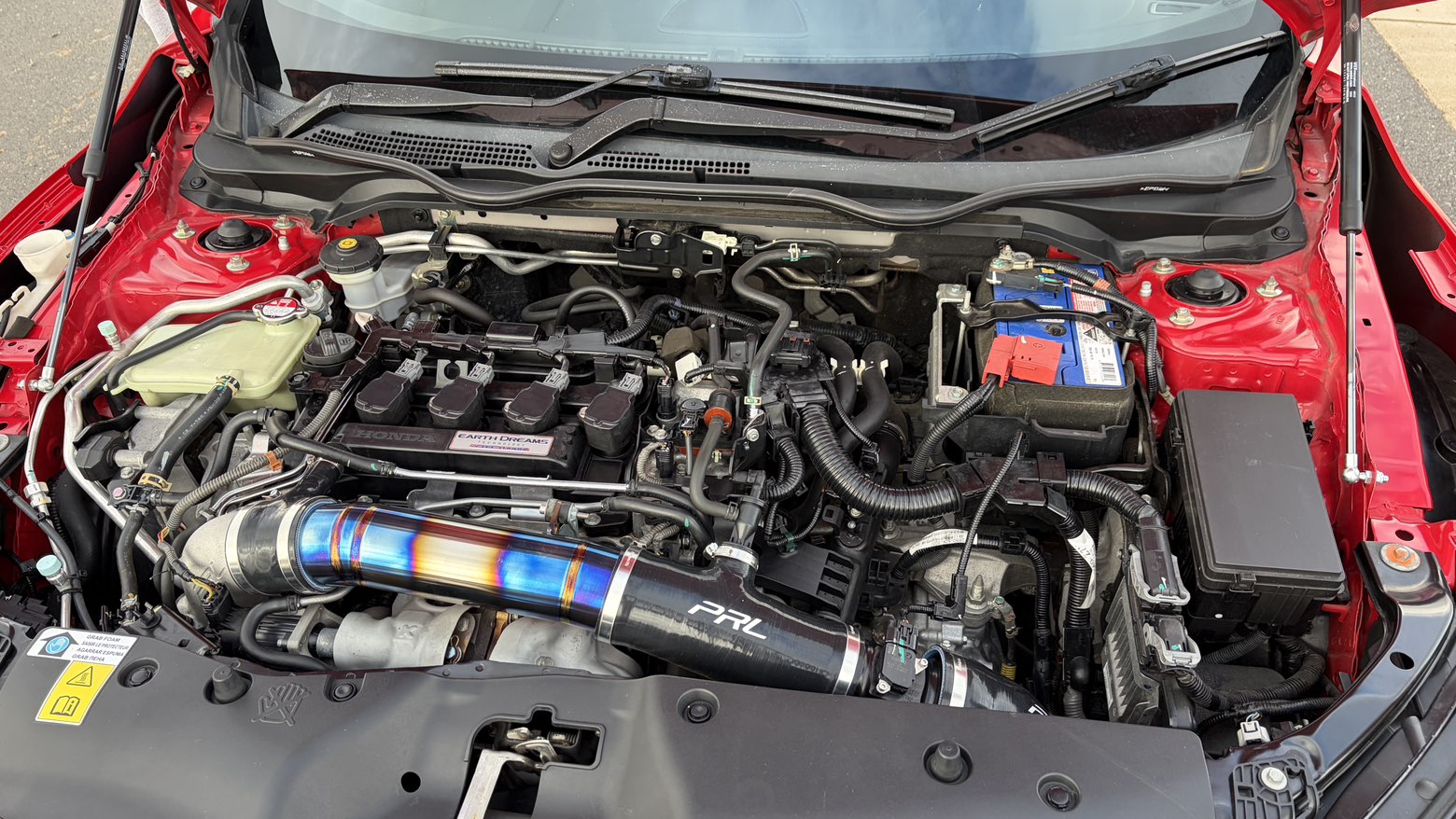 Engine bay of red Honda Civic with titanium intake piping