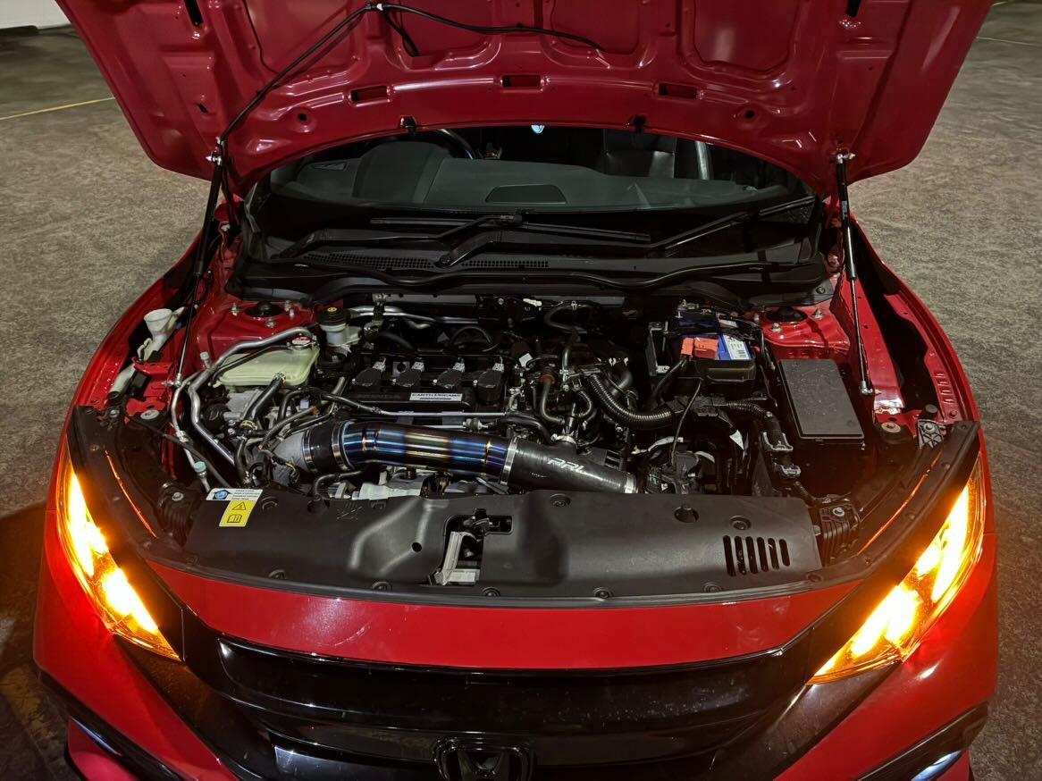 Red Honda Civic hatchback with hood open showing turbo intake, headlights on